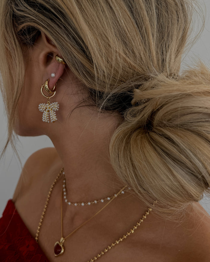 A woman wearing gold and pearl jewelry and a red sweater