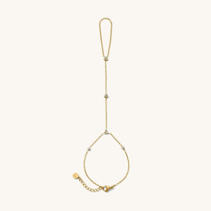 Close up of gold hand chain with stone accents on a white background