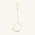 Close up of gold hand chain with stone accents on a white background