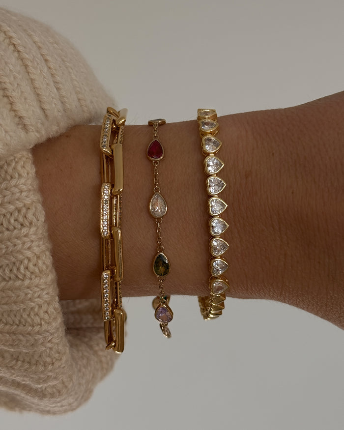 Close up of a wrist with gold and stone bracelets on a white background