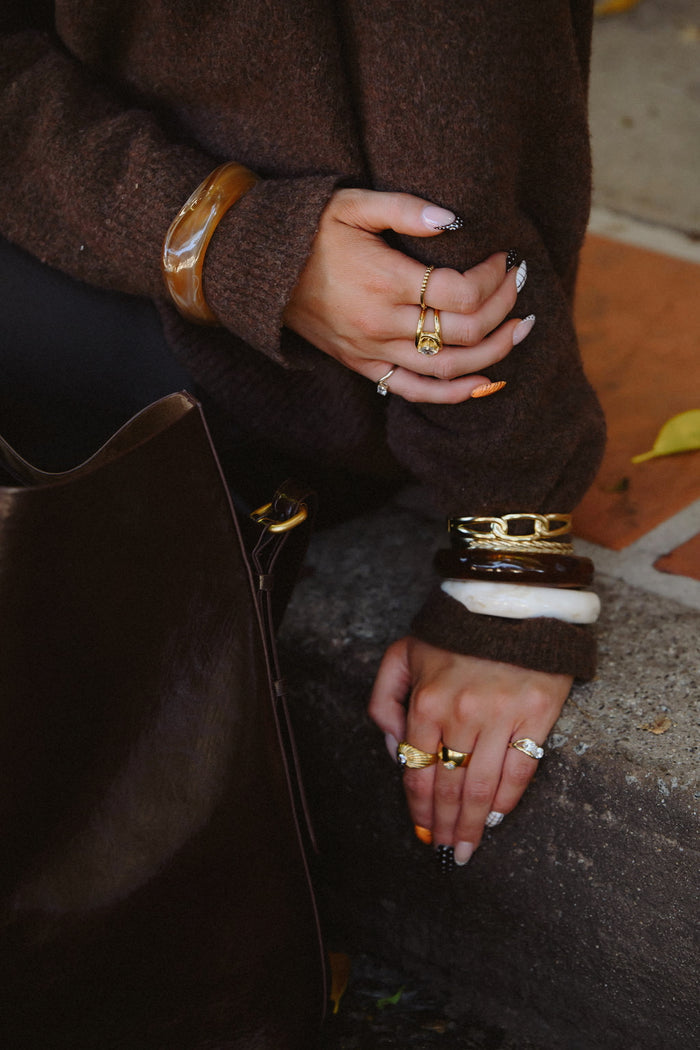 Close up of a person in a brown sweater with gold and resin rings and bracelets