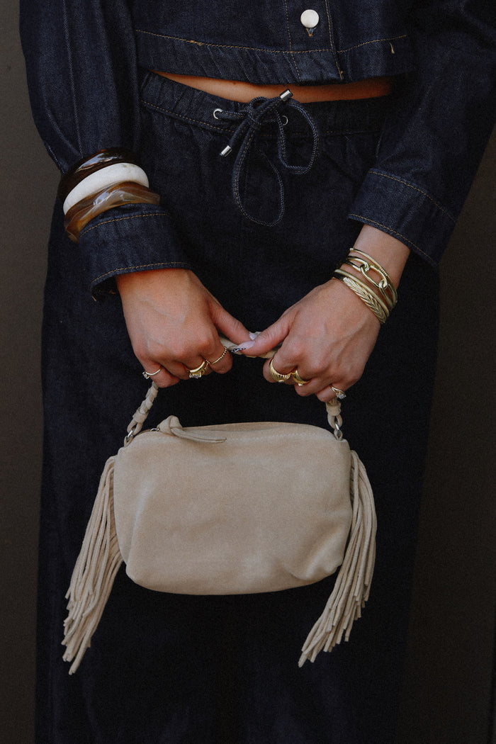 A person in a denim set wearing gold and stone bracelets and rings holding a purse