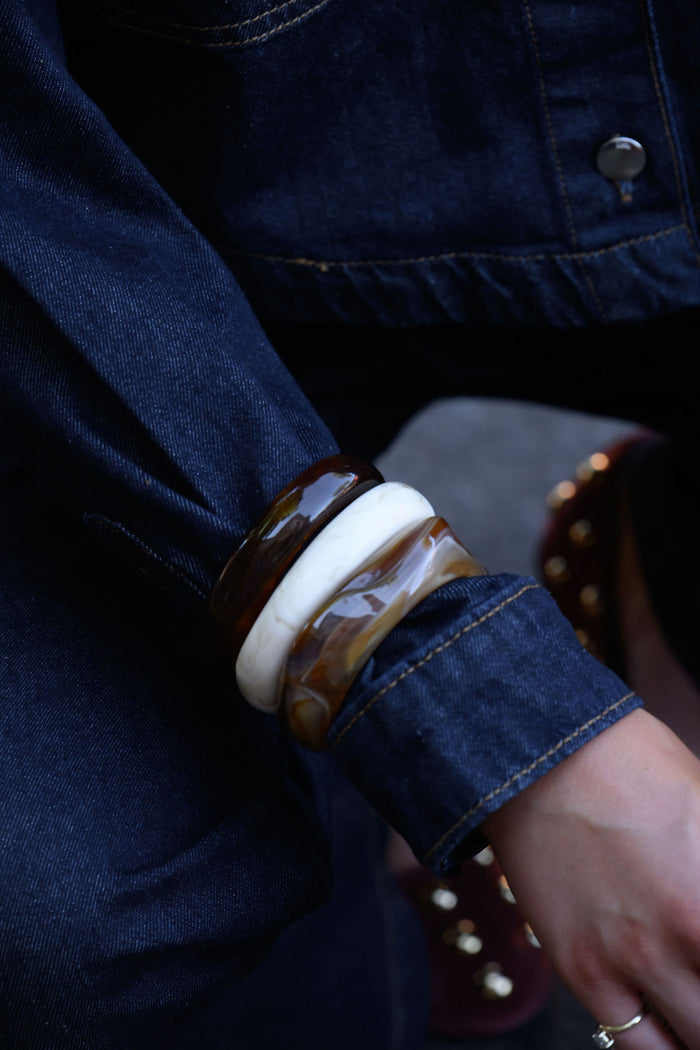 A person in a denim jacket and pants wearing three resin bangles