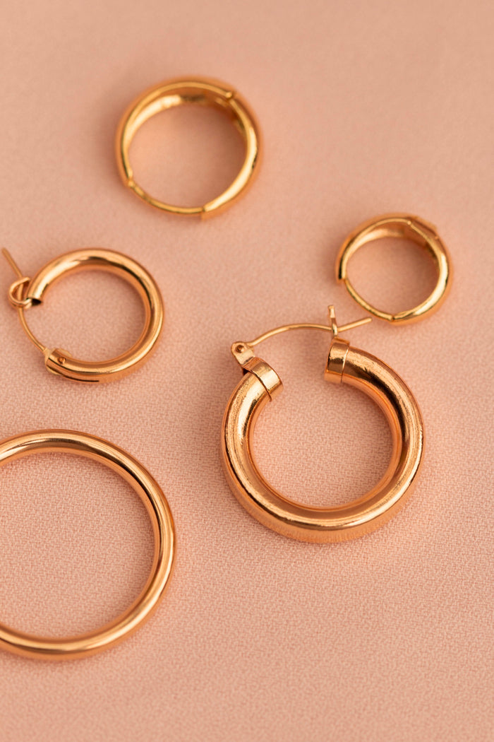 Five gold hoop earrings on a neutral background