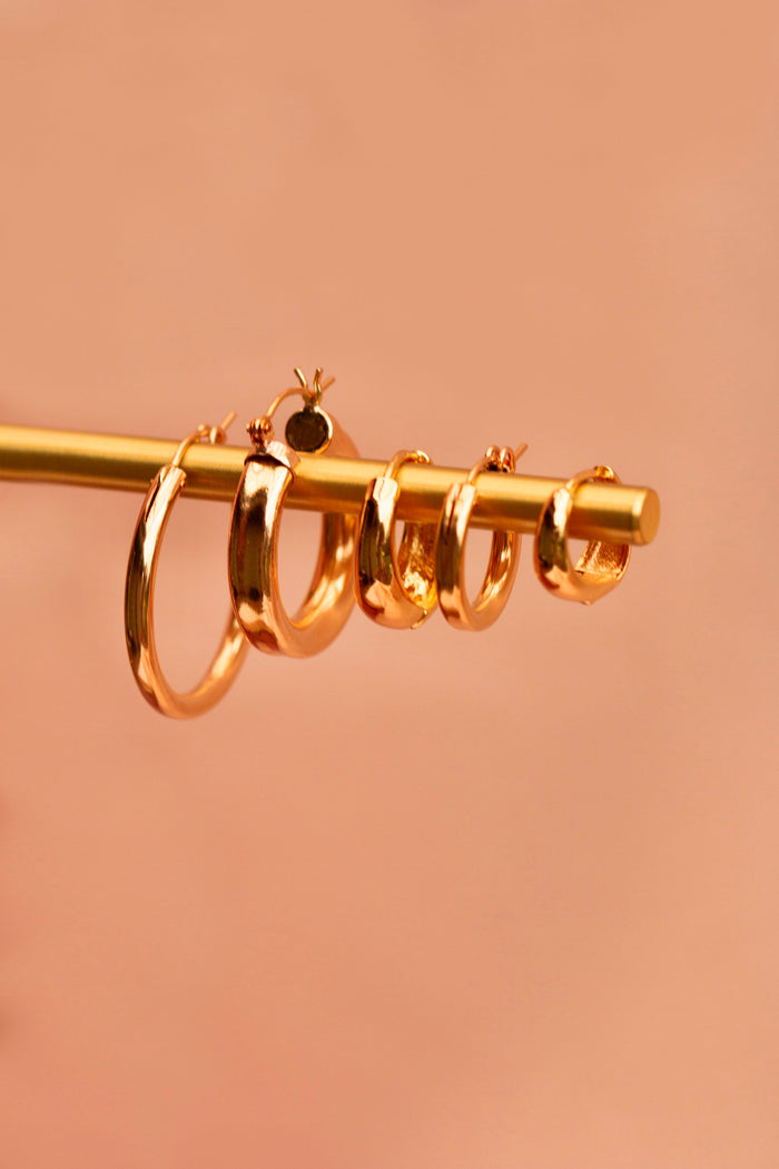 Five gold hoop earrings on a gold jewelry bar against a neutral background