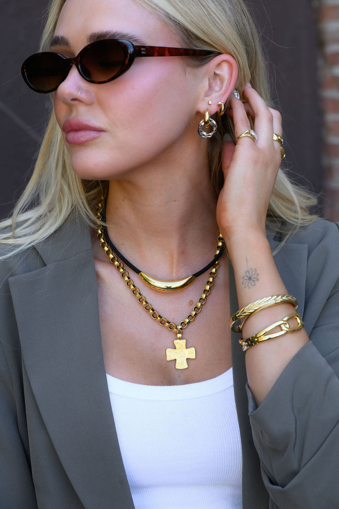 A woman wearing chic gold jewelry and sunglasses in a patterned blazer