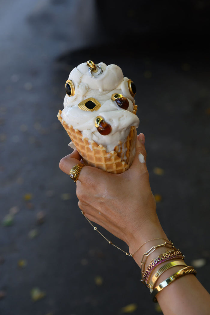 A hand holding an ice cream cone with various gold earrings on top