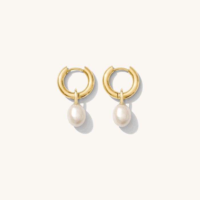 Close up of gold huggie earrings with removable charms on a white background