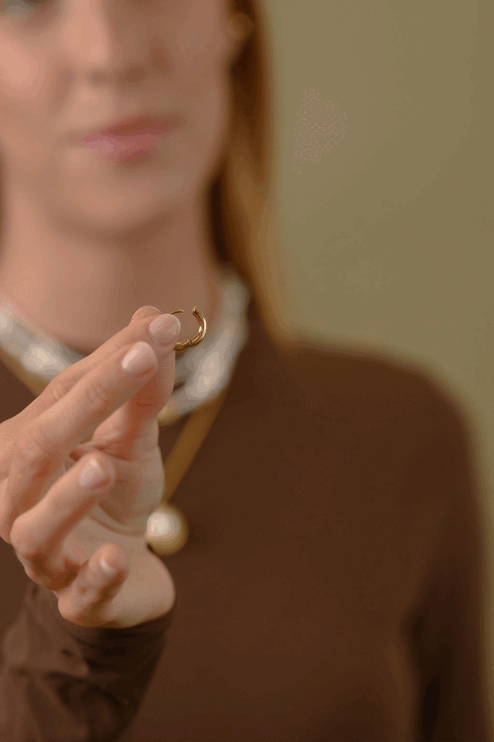 A woman adding a charm to a gold earring