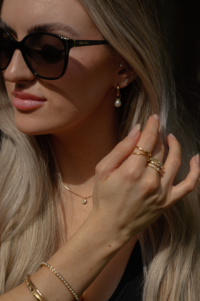 A woman wearing sunglasses, statement earrings, rings, and bracelets