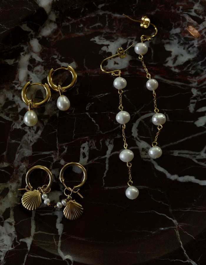 A flat lay of three pairs of pearl earrings on a red marble surface
