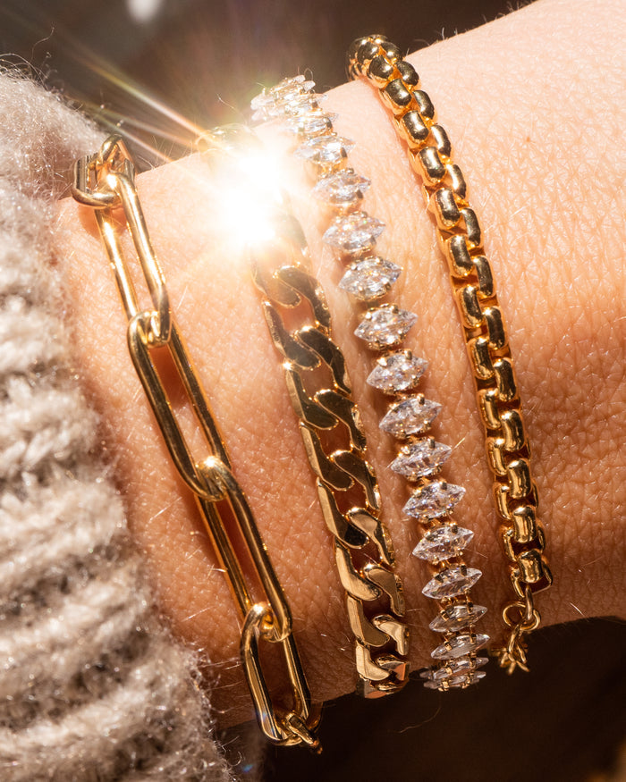 Close up of a wrist with gold and stone bracelets on a brown background