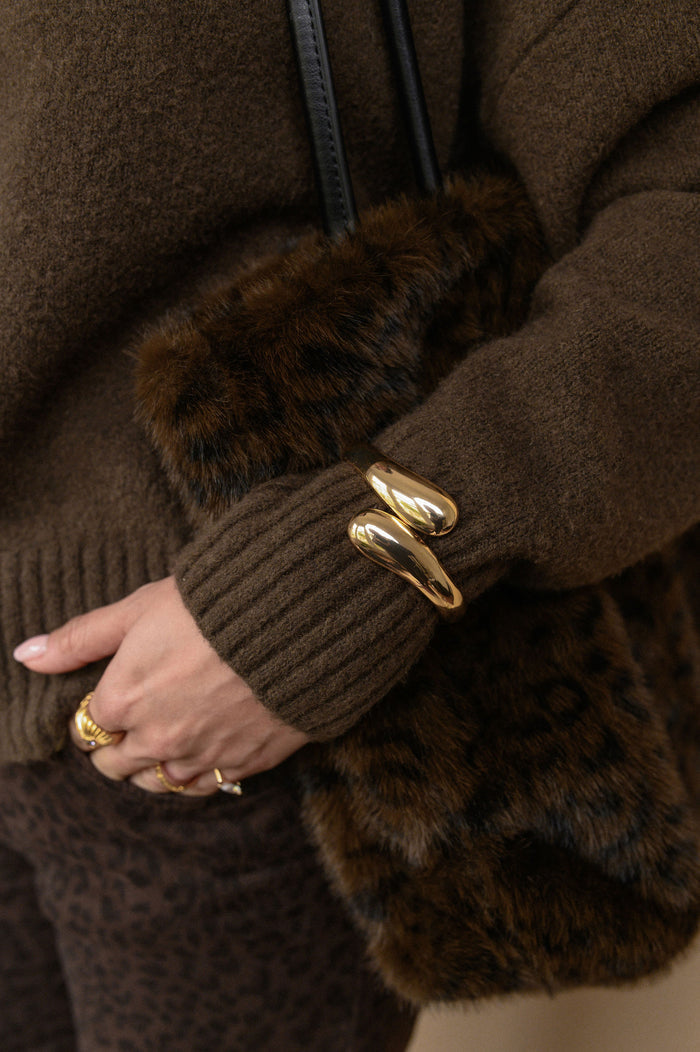 Close-up of a person wearing a brown sweater and fur bag with a gold bracelet.