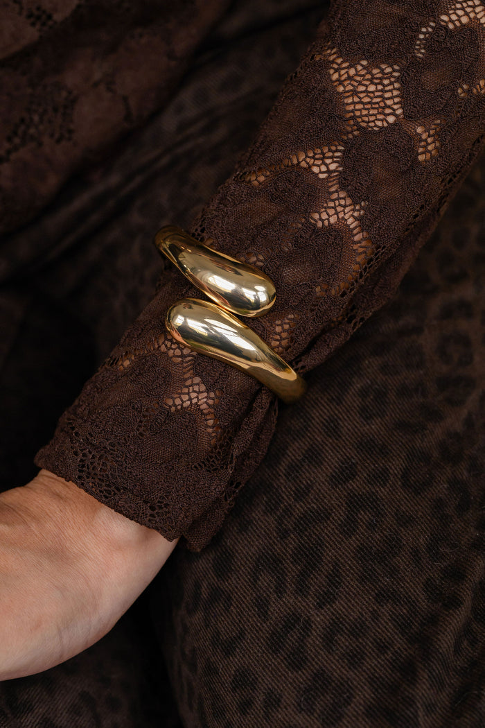 Close-up of a person wearing a brown long sleeve shirt with a gold bracelet.