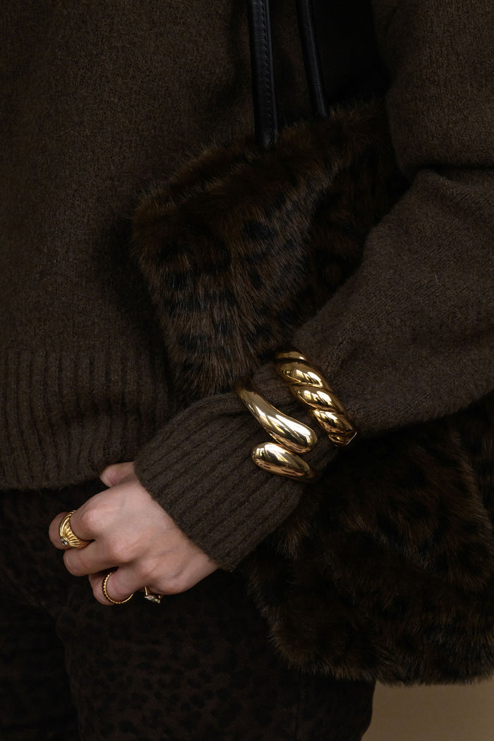 Close-up of a person wearing a brown sweater and fur bag with a gold bracelet.