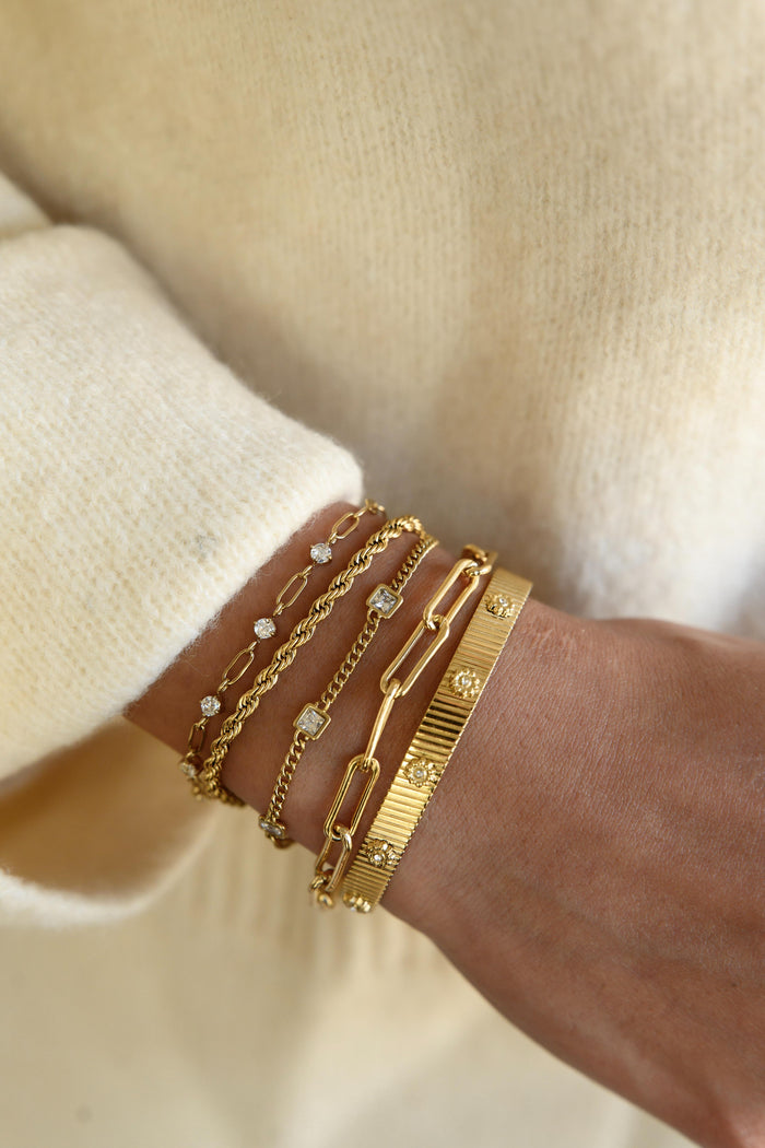A person wearing multiple gold bracelets and a cream sweater