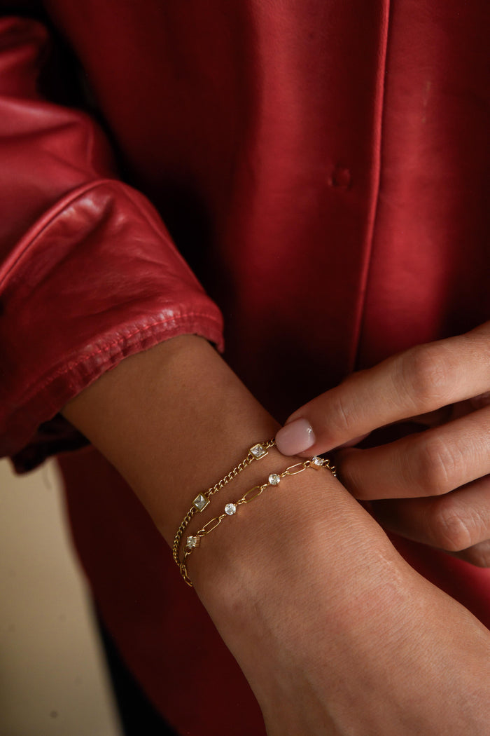 A person in a red shirt wearing two gold bracelets with stone accents