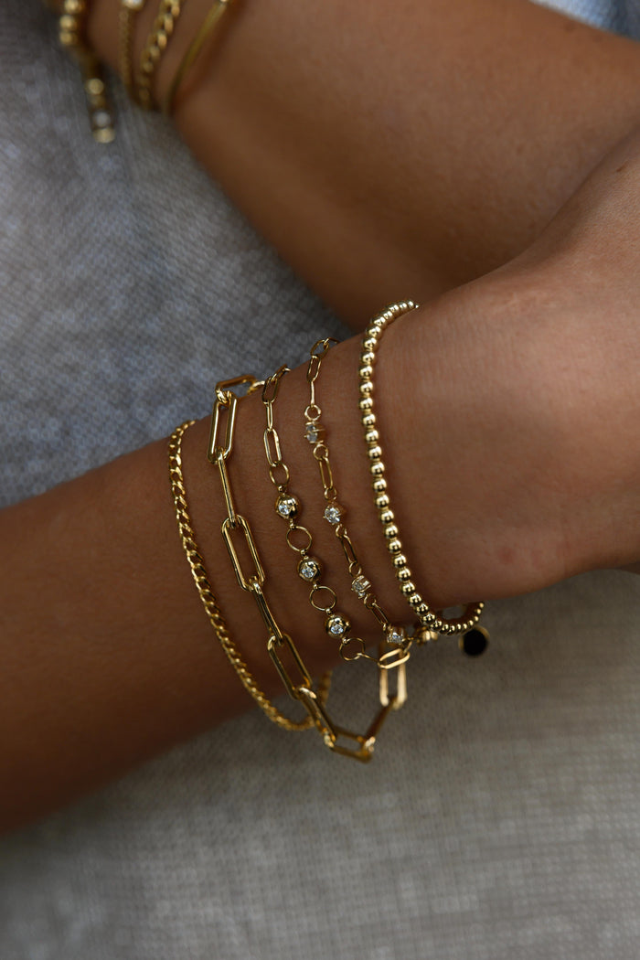 Close up of two wrists with gold bracelets on a dark background