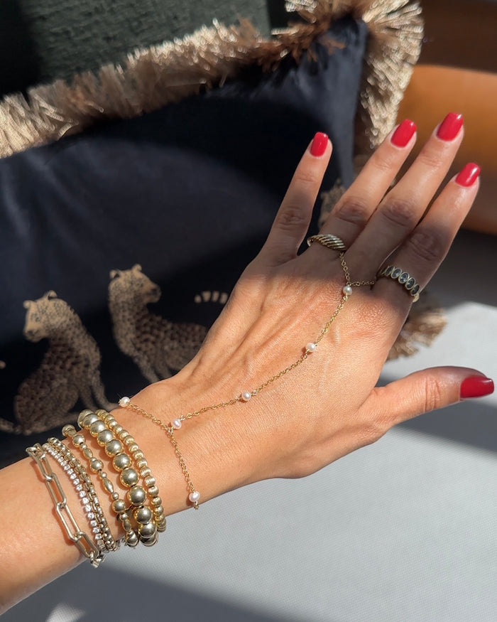 A hand with red nail polish, gold rings, gold bracelets, and a hand chain