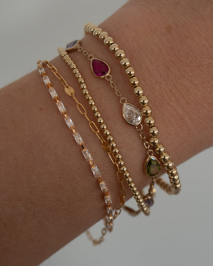 Close up of a wrist with assorted gold and stone bracelets