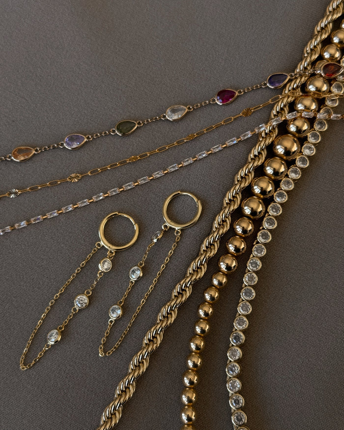 Close up of various gold and stone bracelets and earrings on a taupe background
