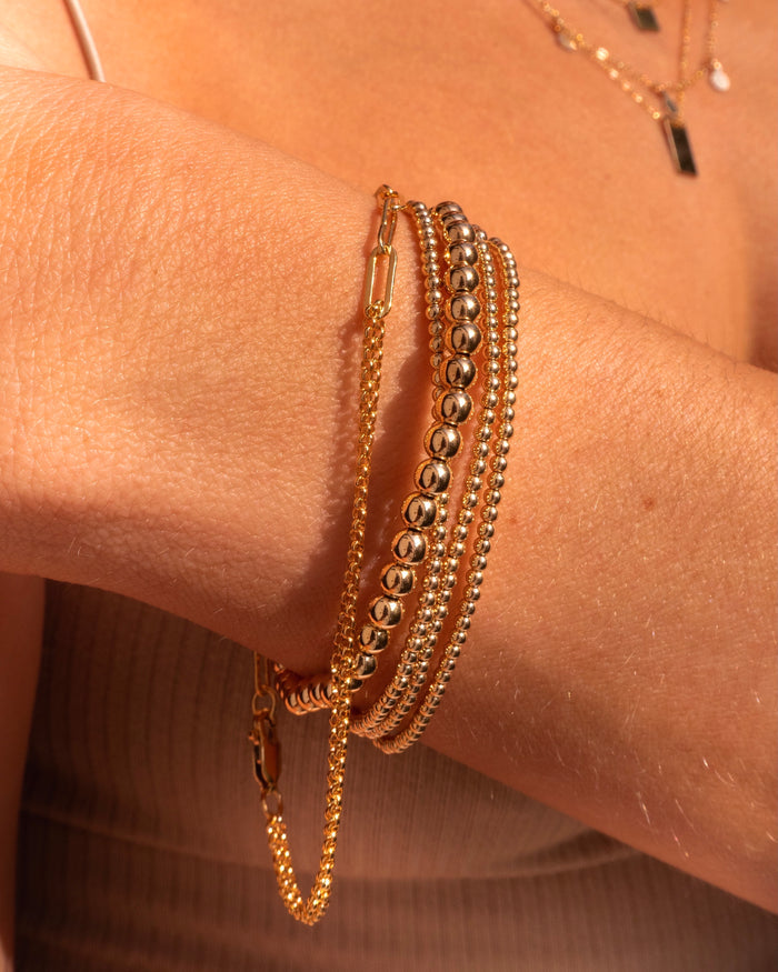 Close up of a wrist with dainty gold bracelets against a person's chest