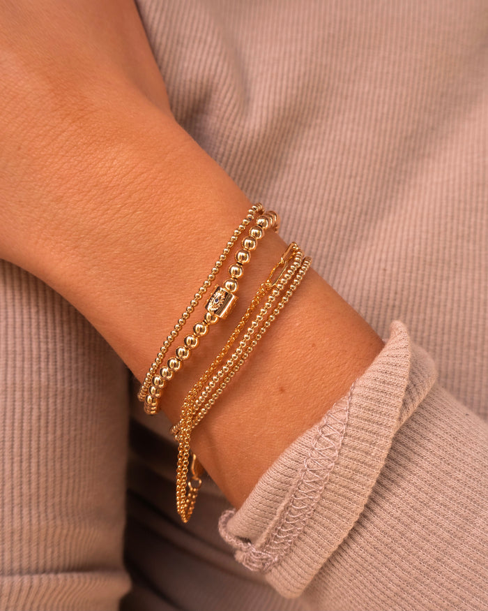 Close up of a person wearing a tan long sleeve shirt with gold bead bracelets