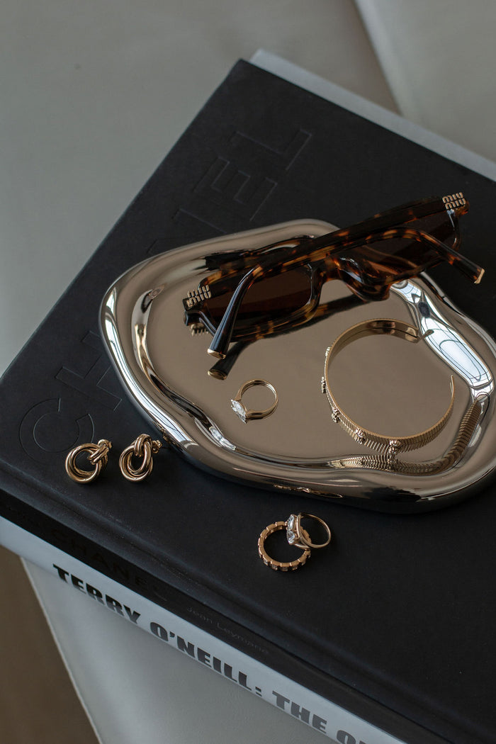 Overhead shot of a pair of earrings, a bangle, rings, a pair of sunglasses, and a silver tray resting on coffee table books