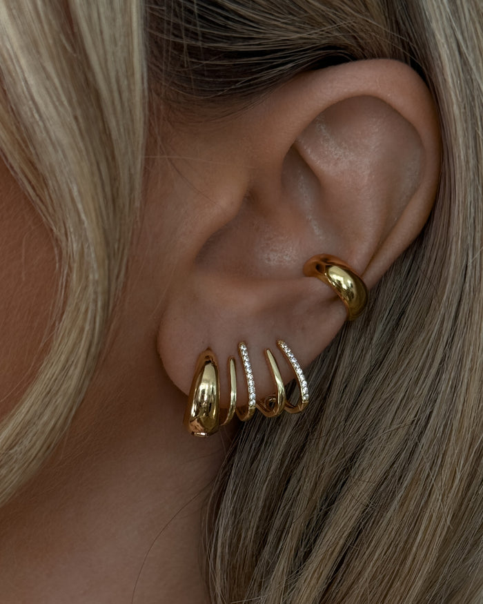 Close-up of an ear with multiple gold and crystal earrings