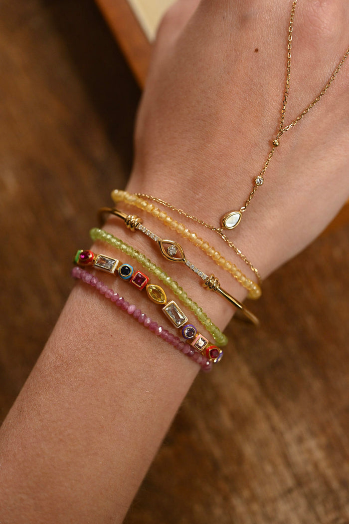 Close-up of a wrist wearing multiple beaded bracelets and a necklace on a wooden surface.