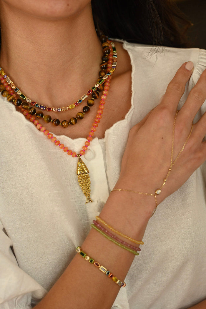 Close-up of a person wearing multiple gold necklaces and bracelets on a neutral background
