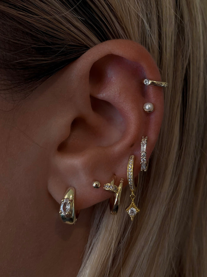 Close-up of an ear with multiple gold, crystal, and pearl earrings