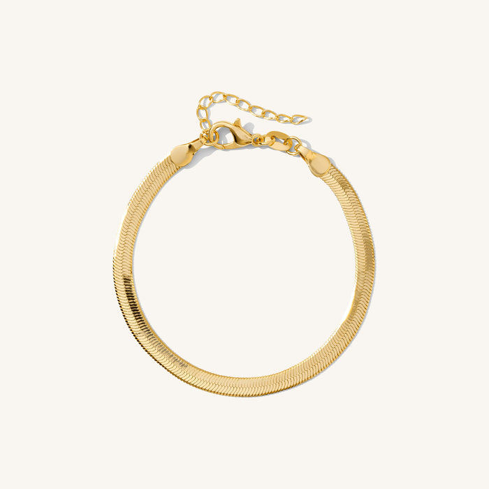 Close up of a gold herringbone bracelet on a white background