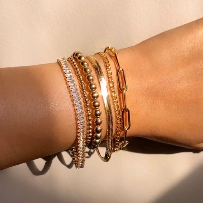Close up of a wrist in a white sweater with gold and stone bracelets resting on a white knit blanket