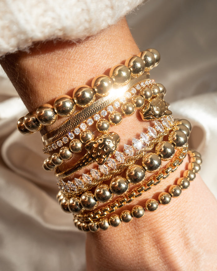 Close up of a wrist with assorted gold and stone bracelets on a white background