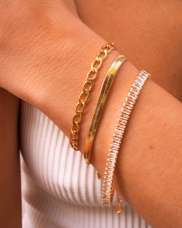 Close up of a person's wrist with gold and stone bracelets against their white tank top