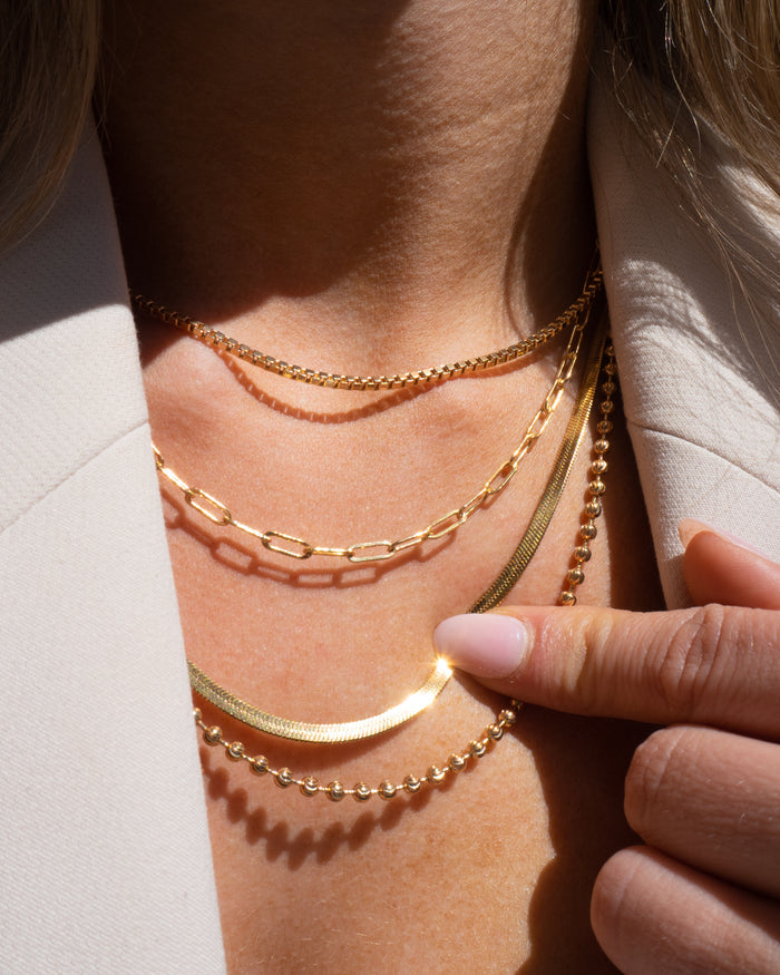 Model wearing the gold Nile herringbone necklace layered with dainty gold chains