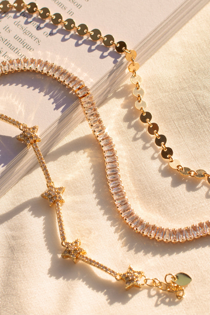 Flatlay of three gold bracelets with stone accents on a tan background
