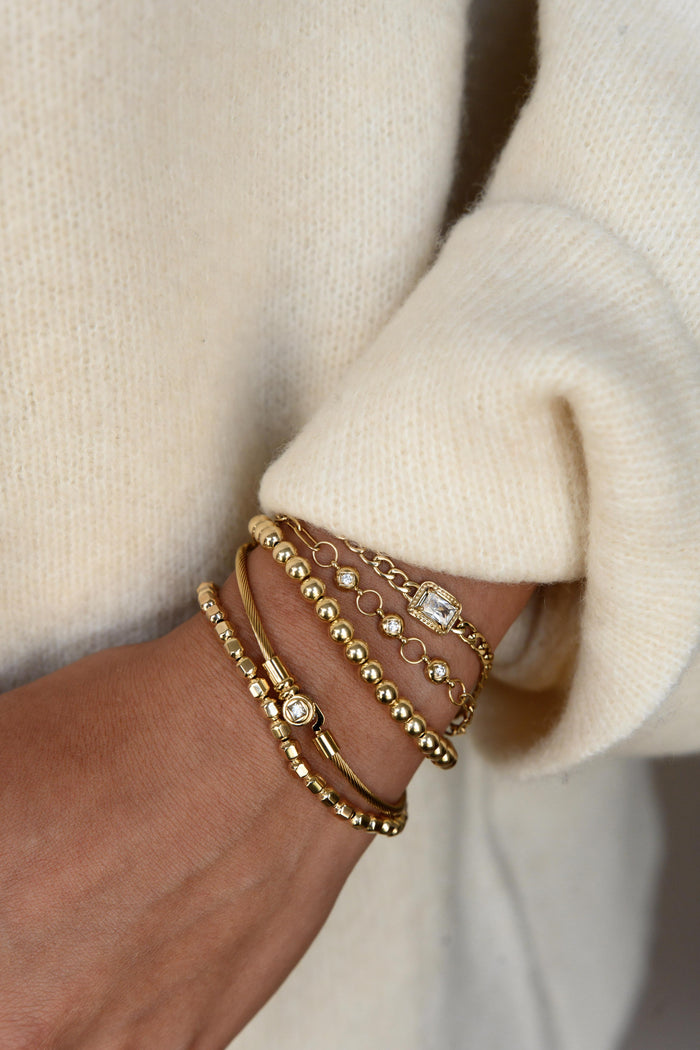 A person wearing multiple gold bracelets and a cream sweater