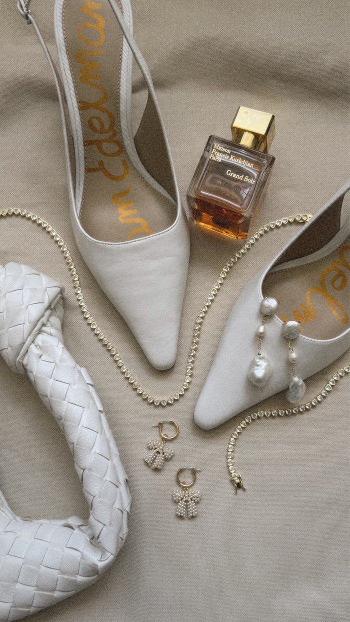 A overhead shot of assorted accessories including shoes and jewelry with fragrance on a tan background.