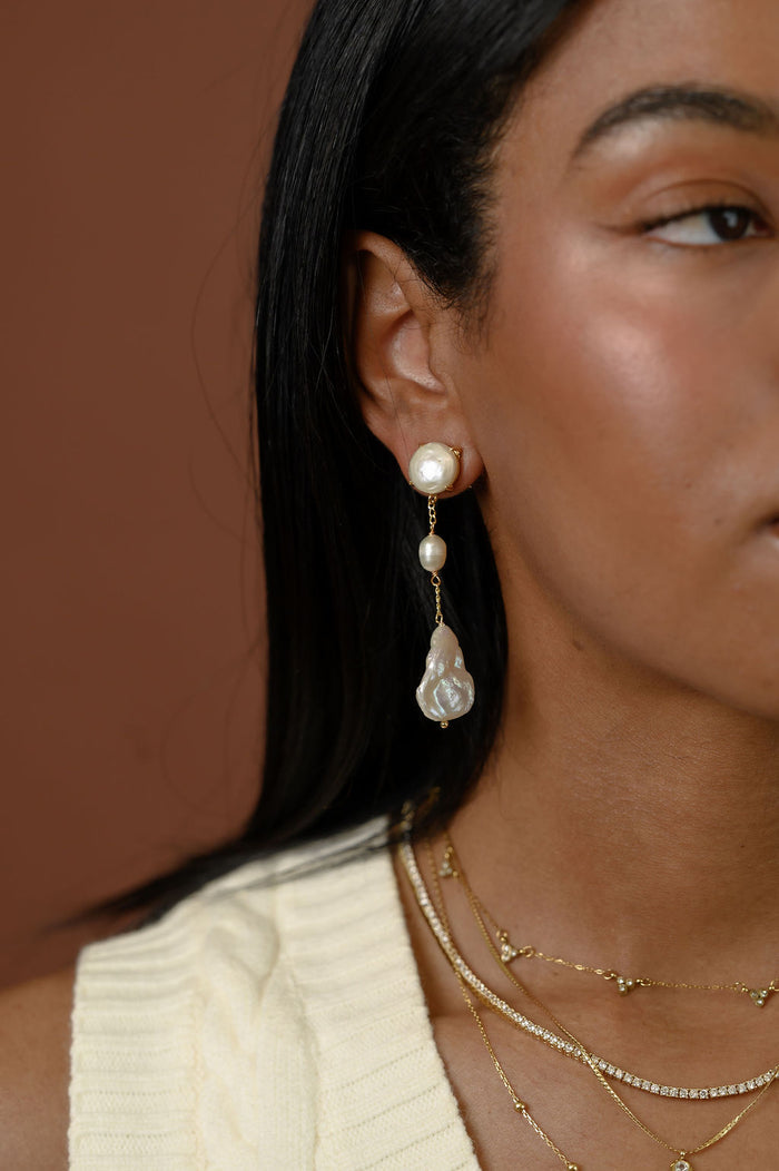 A close up of a woman wearing gold accent earrings and necklaces on a red background
