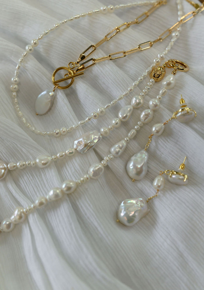 Various pearl jewelry pieces on a white fabric background