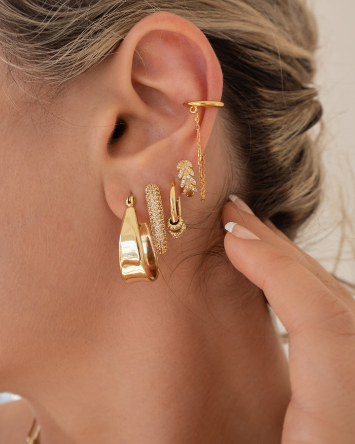 Close-up of an ear with multiple gold and crystal earrings