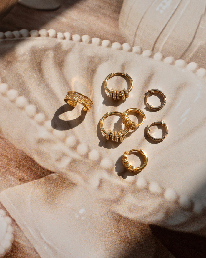 Three pairs of gold hoops with crystal accents on a shell painting