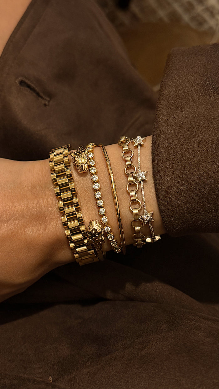 Close up of a wrist with a brown jacket and assorted gold and stone bracelets
