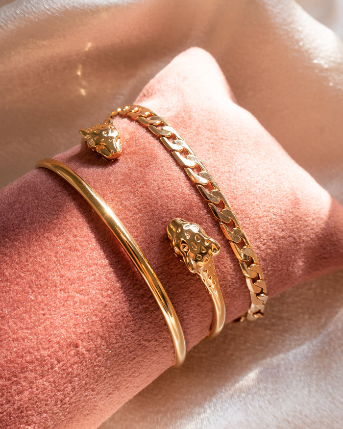 Close up of gold bracelets on a pink jewelry pillow against a white background