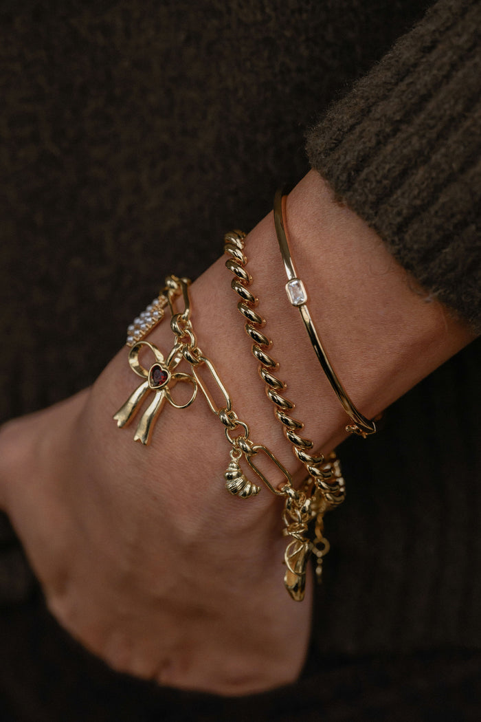 Gold bracelets with charms on a wrist against a dark background