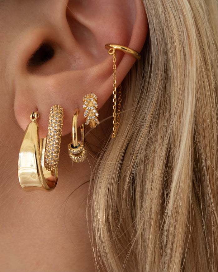 Close-up of an ear with multiple gold and crystal earrings