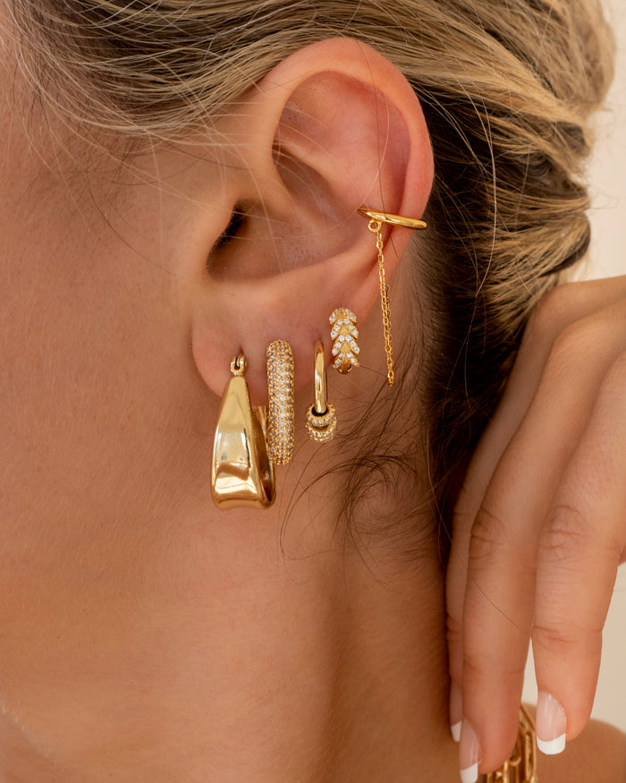 Close-up of an ear with multiple gold and crystal earrings