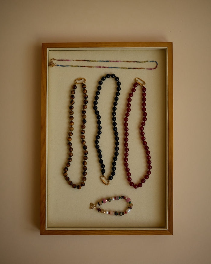 Jewelry display with necklaces in a wooden frame on a beige wall.